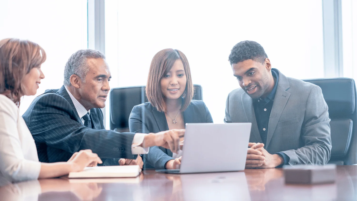 Four businesspeople in a conference room leaning in around a laptop