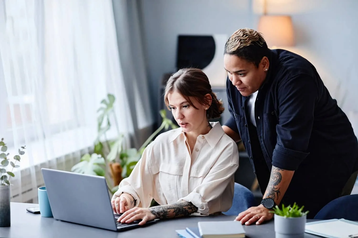 Two tattooed colleagues working through something together at a laptop in a bright office