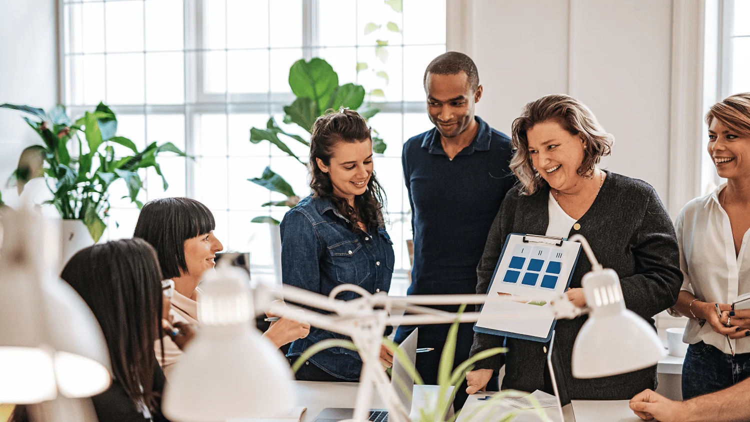 A team gathered around a desk while a colleague walks them through a chart on a clipboard