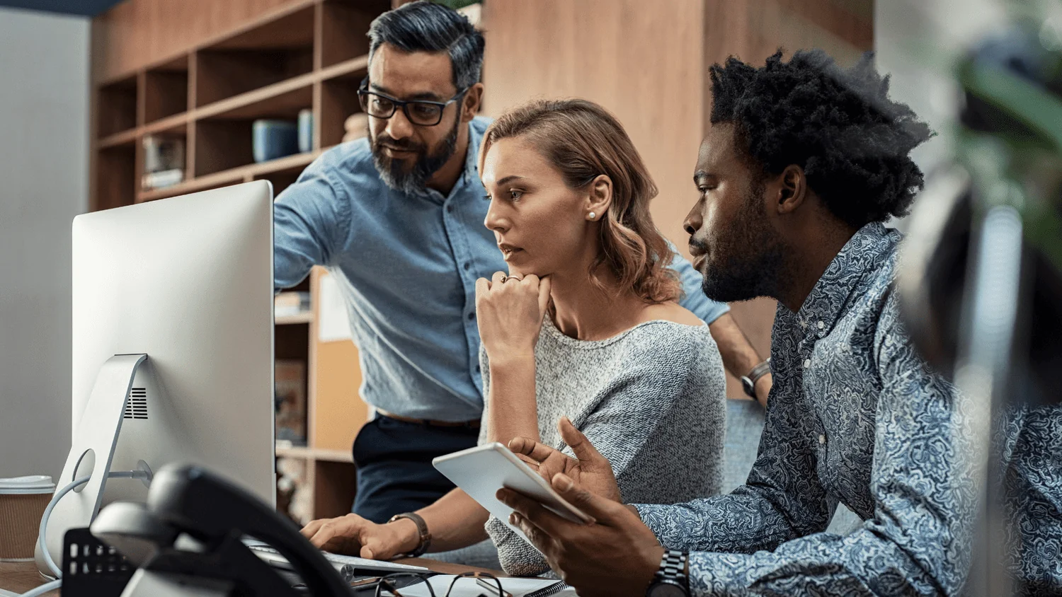 Three colleagues carefully reviewing content together on a desktop monitor